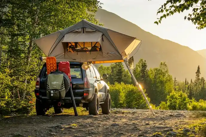 SUV with a rooftop tent at a forest campsite.
